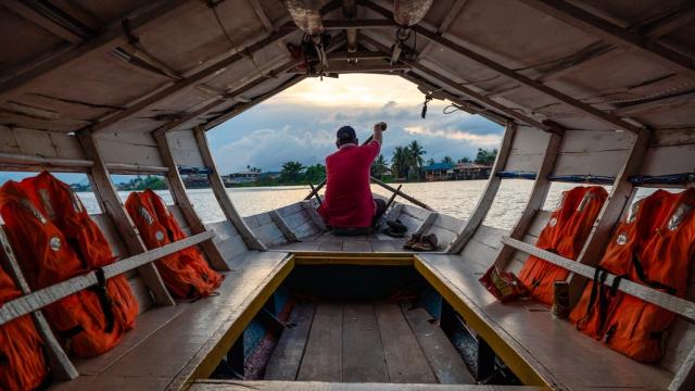 A man on a tourist boat paddles toward shore in Sarawak.